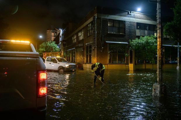 Un trabajador desbloquea los desagües en una calle afectada por las inundaciones en Brooklyn, Nueva York, a principios del 2 de setiembre de 2021. (Ed JONES / AFP).
